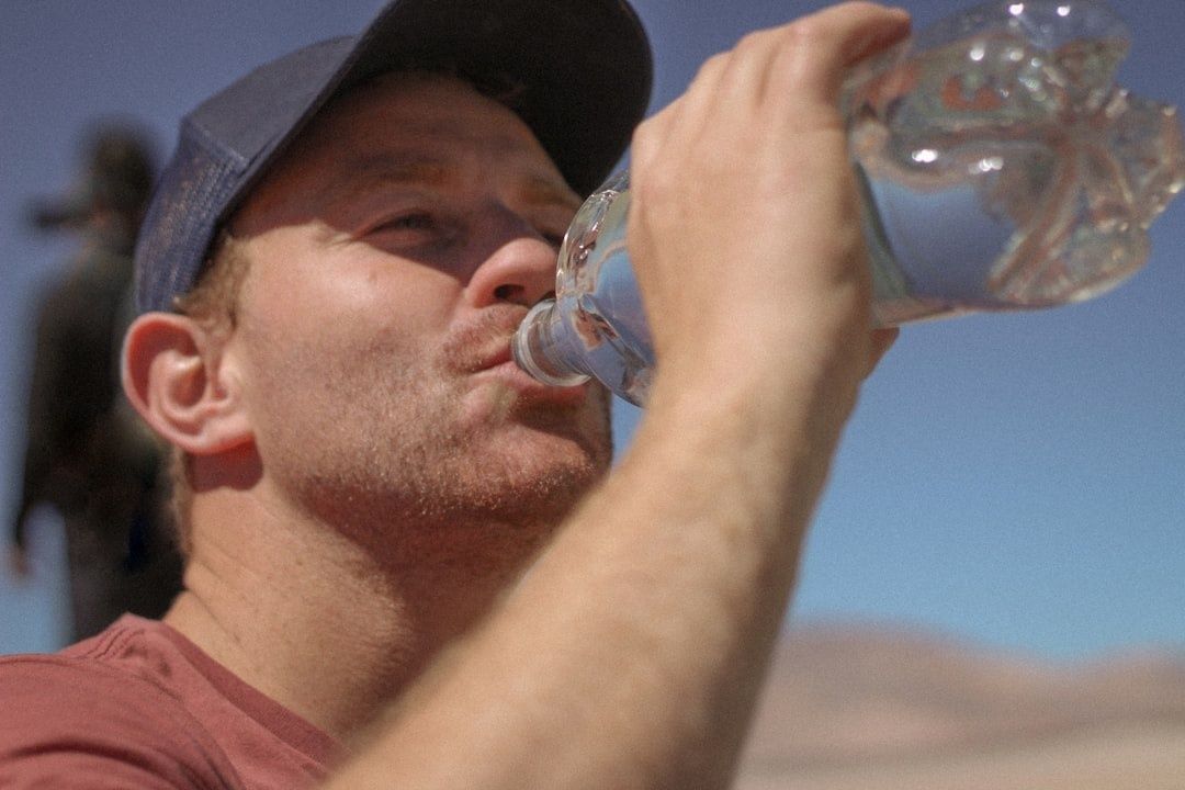 Person i keps dricker vatten ur en genomskinlig flaska utomhus